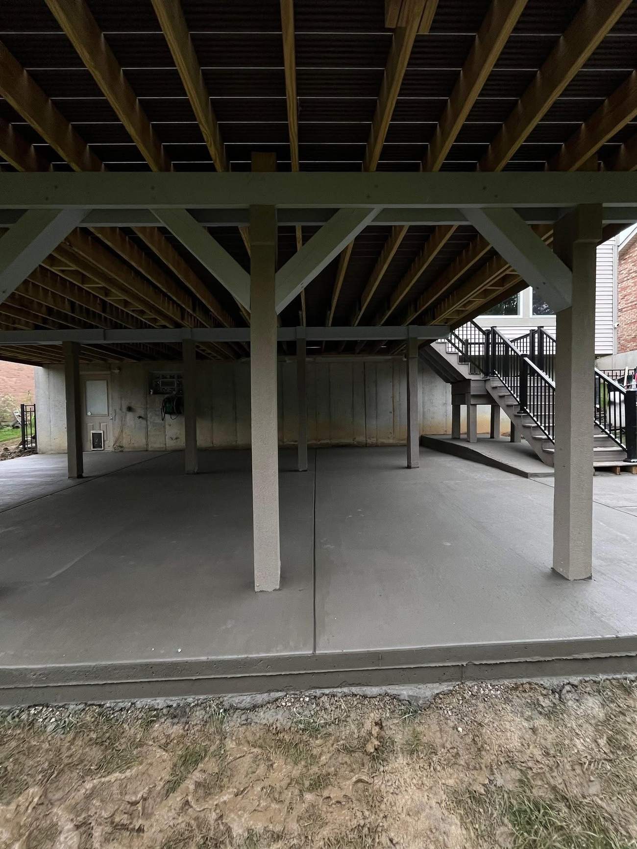 Large finished concrete patio beneath a raised deck, second angle