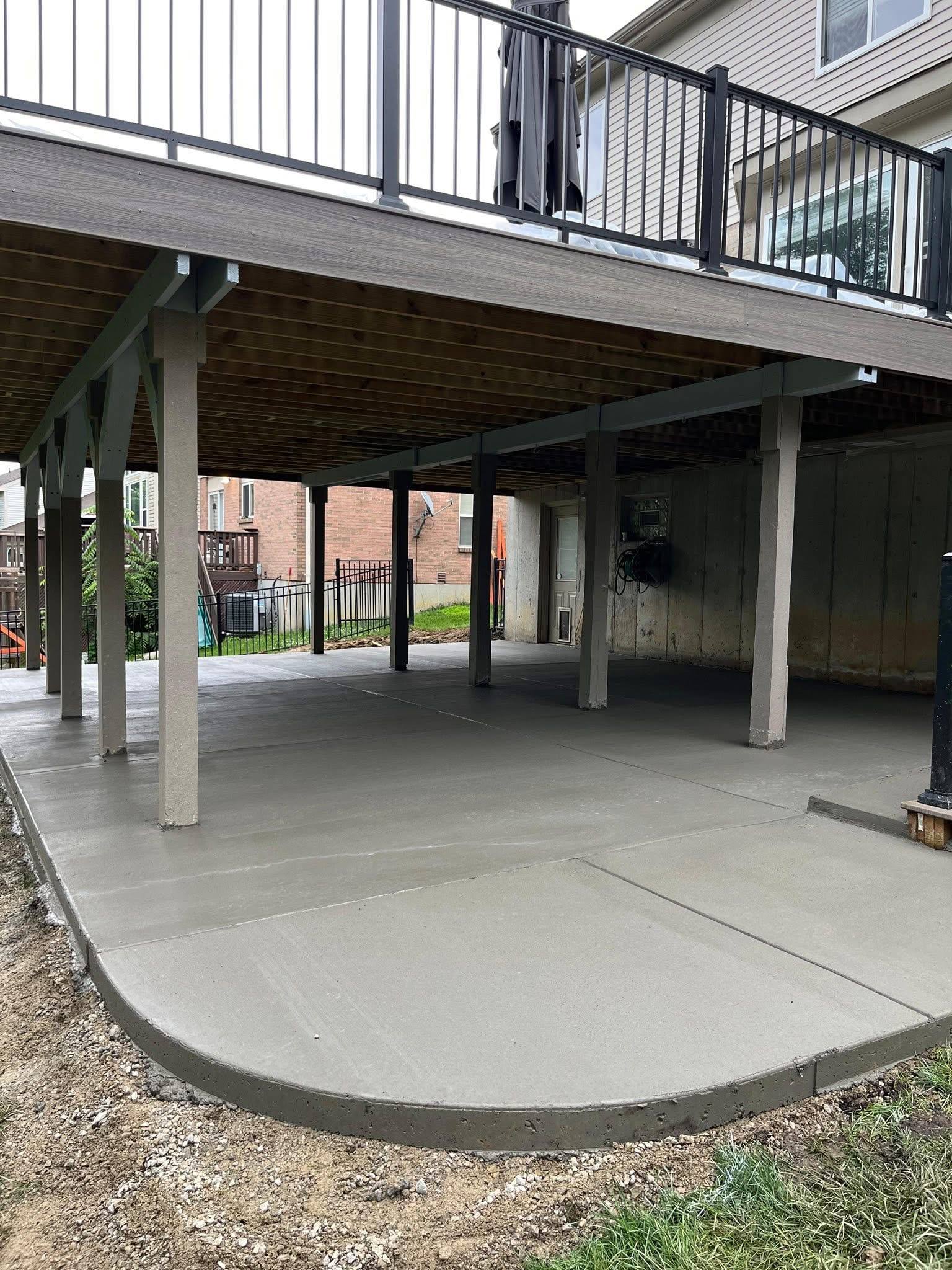 Large finished concrete patio with curved edge beneath a raised deck